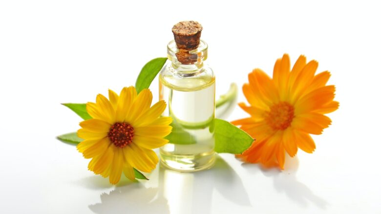 A bottle of essential oil and a flower on a white surface.